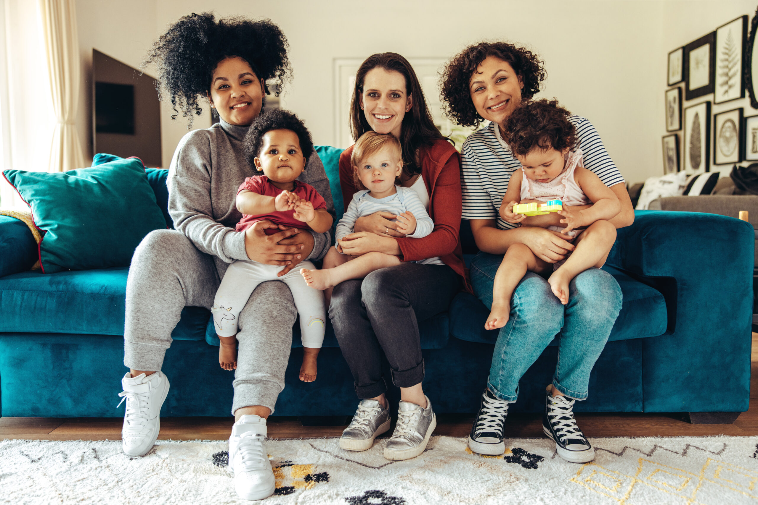 Friendly moms with babies sitting on sofa at home. Club of young mothers.